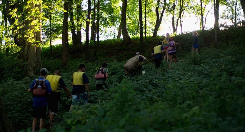 A group of people wearing life jackets hike through a green wooded area